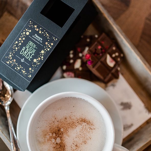 Kaffeetasse auf Holztisch mit angebrochenen dunkle Schokoladentafel mit gefriergetrockneten Früchten und dazugehörige schwarzer Verpackung